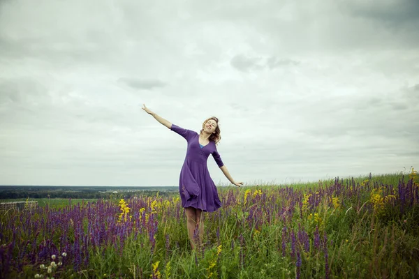 Young girl in vintage dress walking through sage flower field.