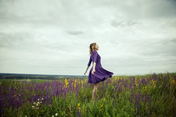 Young girl in vintage dress walking through sage flower field.