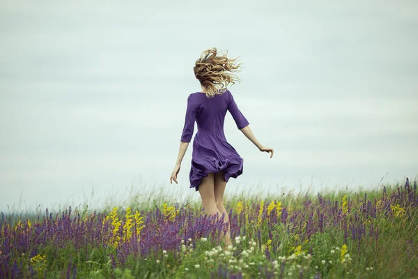 Young girl in vintage dress walking through sage flower field.