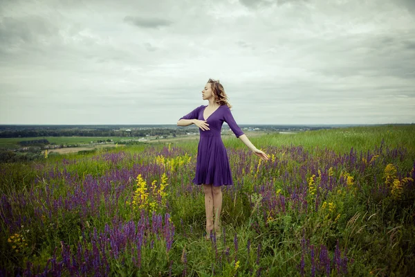 Young girl in vintage dress walking through sage flower field.