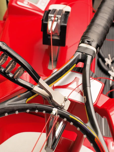 Tennis racquet on a stringing machine with the first main strings end secured by a starting clamp.