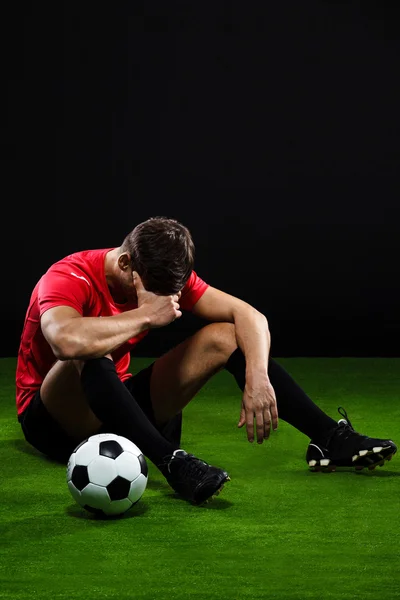 Soccer player with ball sitting on grass over black background
