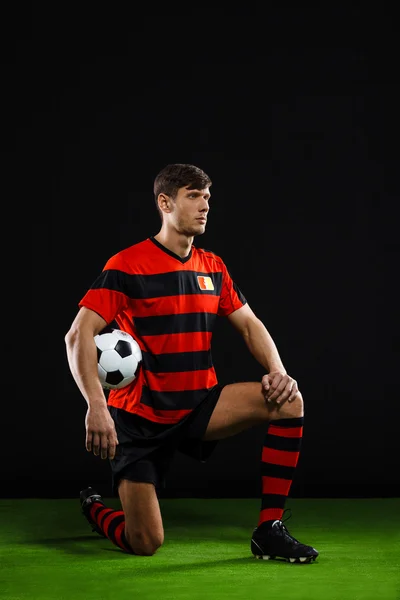 Soccer player with ball standing on one knee over black backgrou