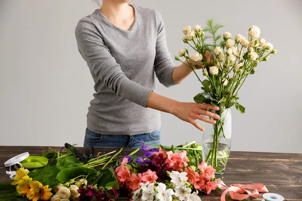 Girl make bouquet over gray background, putting flowers in vase.