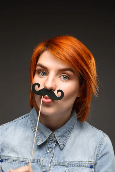 Portrait of young girl wearing fake mustache over grey backgroun