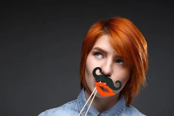 Portrait of young girl wearing fake mustache and lips over grey