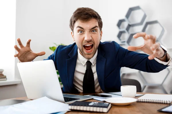 Angry young businessman shouting, office background.