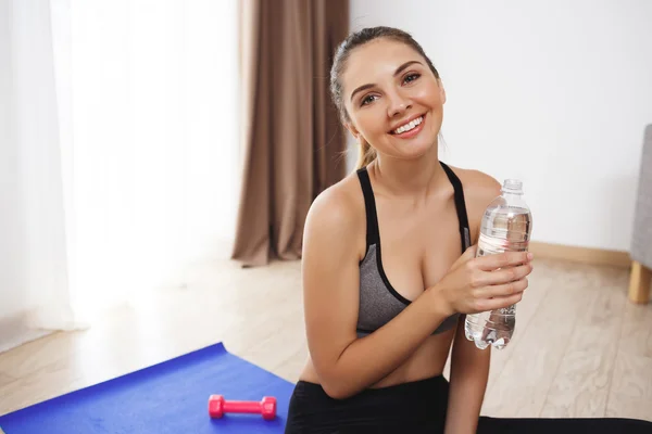 Cheerful young fitness girl make yoga execises on floor and drink water