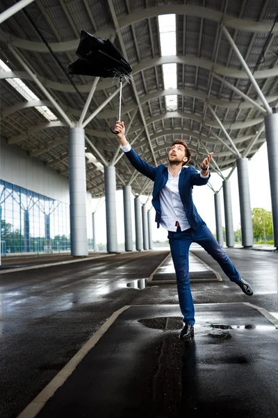 Picture of young businessman on rainy station background catching broken umbrella