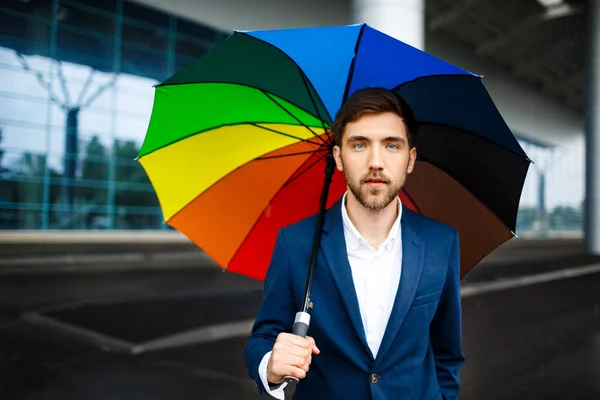 Picture of  confident young handsome businessman holding motley umbrella in the street