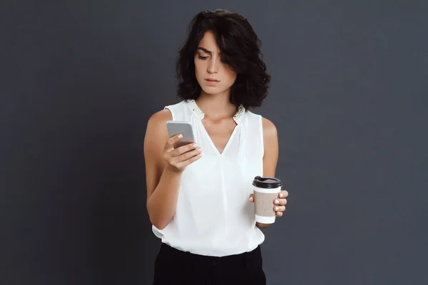Confused young woman holding her phone and coffee in hands