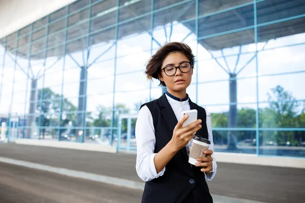 Young successful businesswoman looking at phone, standing near business centre.