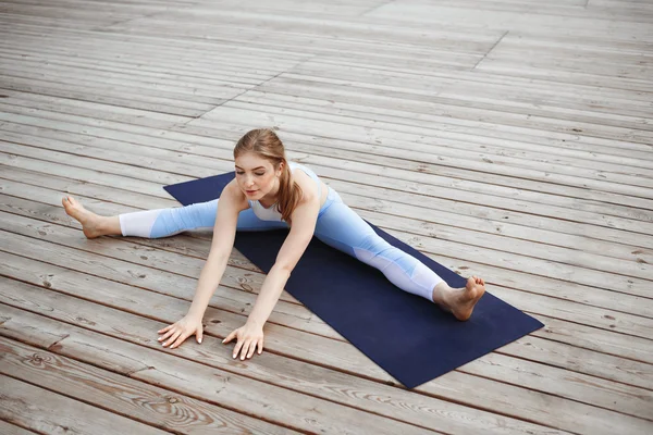 Young beautiful blonde girl practicing yoga outside.