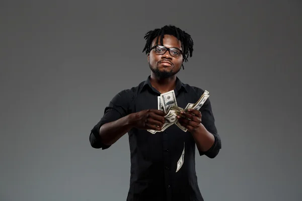 Young successful african businessman throwing money over dark background.