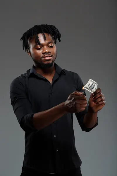 Young successful african businessman burning money over dark background.