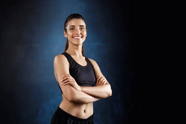 Beautiful sportive girl posing with crossed arms over dark background.