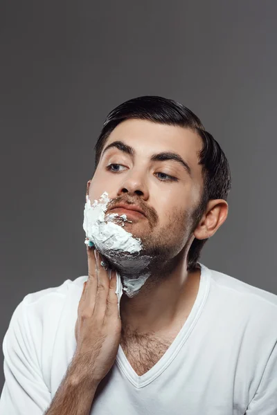 Man applying cream for shave on face over grey background.