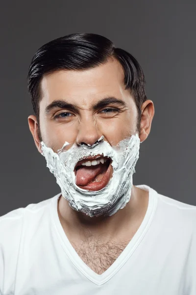 Man applying cream for shave on face over grey background.