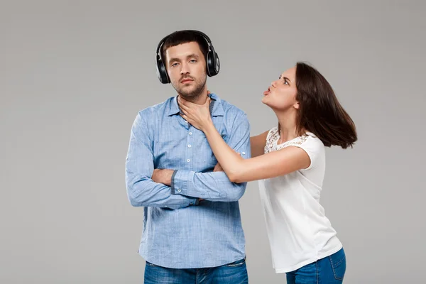 Young woman angering with man in headphones over grey background.