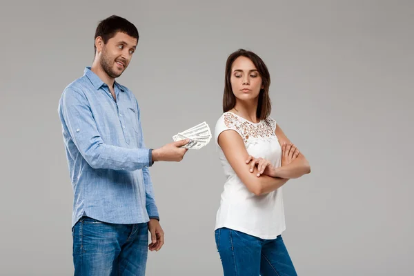 Young man giving money to woman, smiling over grey background.