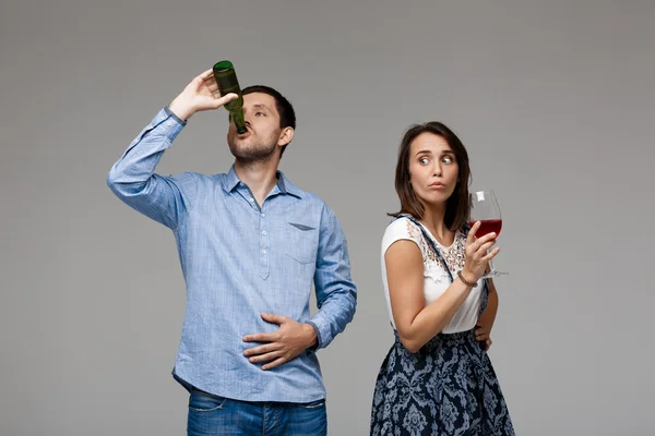 Young beautiful couple drinking wine and beer over grey background.