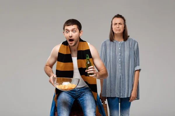 Man drinking beer, watching football, upset woman standing behind, crying.