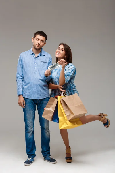 Young woman holding purchases, taking last money from man.