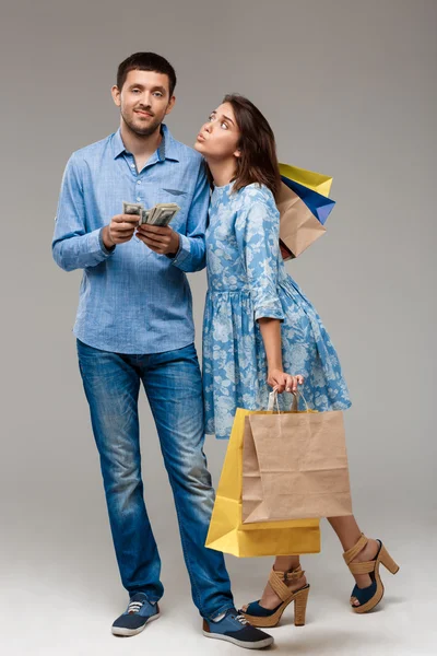 Young woman with purchases, man holding money over grey background.