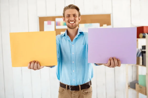 Young handsome cheerful smiling businessman holding colored folders. White modern office interior background.