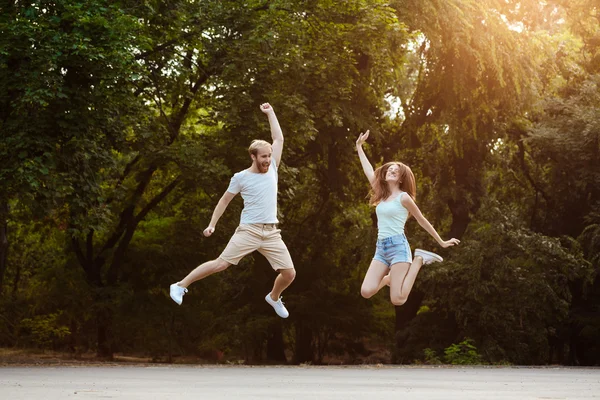 Young beautiful couple jumping, smiling, rejoicing, walking in park. Outdoor background.