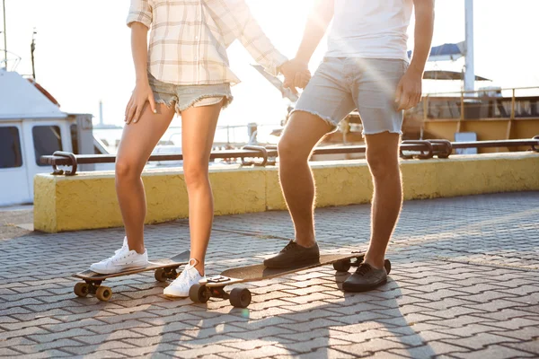 Young beautiful couple walking at seaside, skateboarding. Close up of legs.