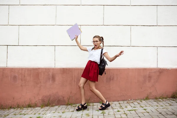 Young beautiful female student in glasses walking down street, holding folders.