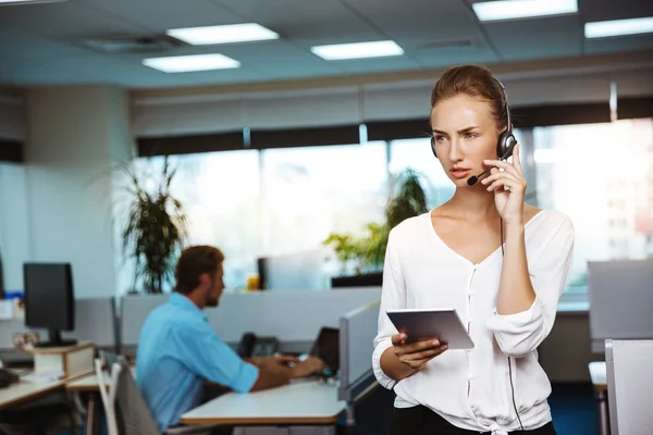 Young beautiful female support phone operator speaking, consulting, over office background.