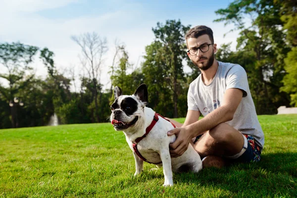 Handsome man sitting with french bulldog on grass in park.