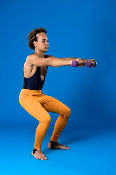 Sportive african man training with dumbbells over blue background.