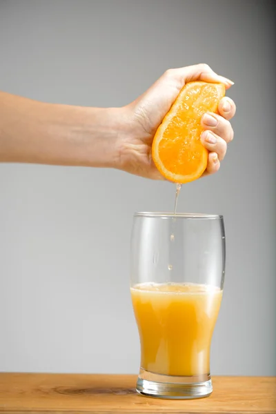 Girl s hand squeezing out juice from orange into glass.