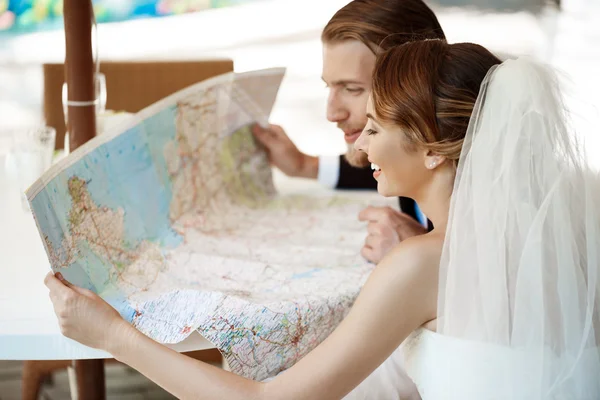 Young beautiful newlyweds smiling, choosing honeymoon trip, looking at map.