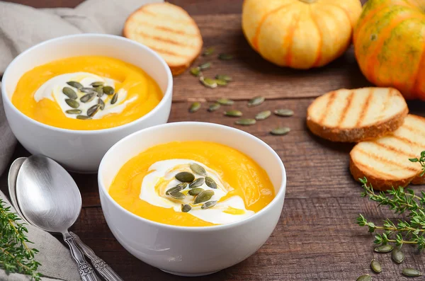Pumpkin cream soup with cream and pumpkin seeds on wooden background