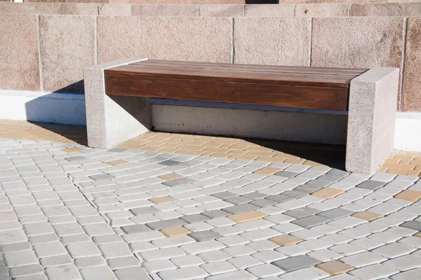 Wooden bench with stone foundation in middle of paving slabs.