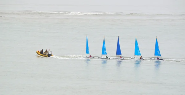 Five small Colourful Sailing Dinghies being towed by a small inflatable power boat.