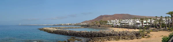: Panorama of the western end of Playa Blanca promenade with holiday makers on the man made Flamingo beach and the lighthouse.