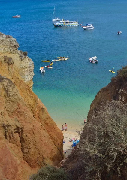 Tiny Beach at the bottom of sea cliffs with holiday makers and tourist boats Lagos Portugal.