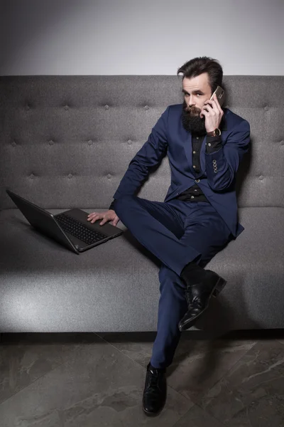 Bearded man dressed in suit and with laptop and talk on phone;