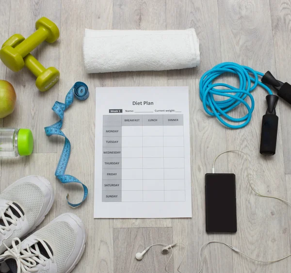 Various sport equipment with diet plan on wooden background