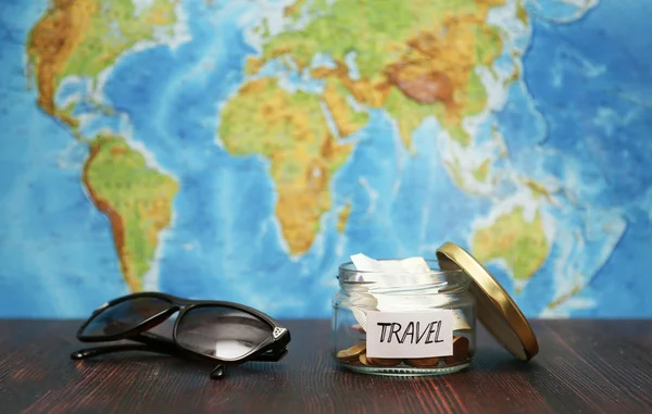 Travel money in  jar, sunglasses, world map at  background.
