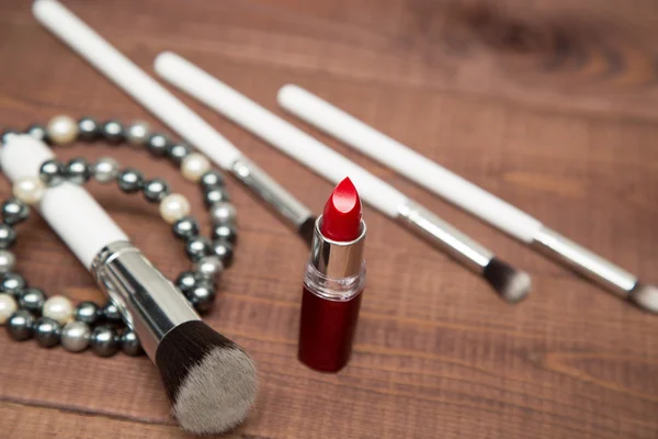 Makeup items brushes and lipstick, scattered across a wooden surface