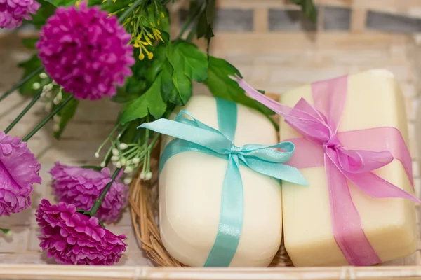 Two soaps with bows in wooden busket with purple flowers