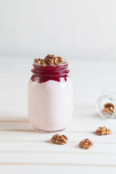 Homemade yogurt with jam and walnuts in a jar on a white wooden