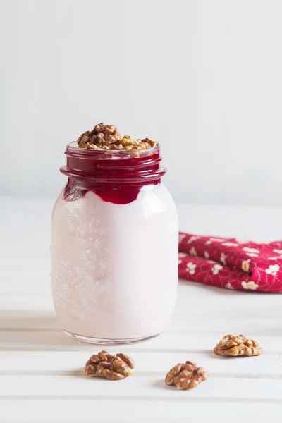 Homemade yogurt with jam and walnuts in a jar on a white wooden