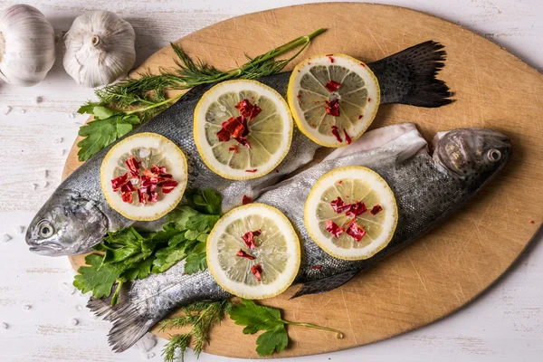 Fish dish cooking with various ingredients. Raw rainbow trout with lemon, garlic ,herbs and spices on cutting board , top view. Healthy food or diet nutrition concept